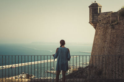 Rear view of woman standing by railing against sea