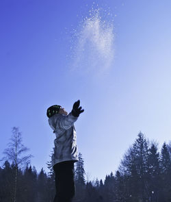 Low angle view of boy throwing snow while standing against clear blue sky