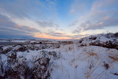 Snow covered field against sky during sunset