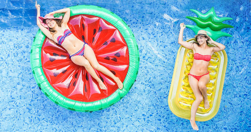 High angle view of female friends relaxing on inflatable rings in swimming pool