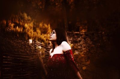 Young woman looking away while standing against trees