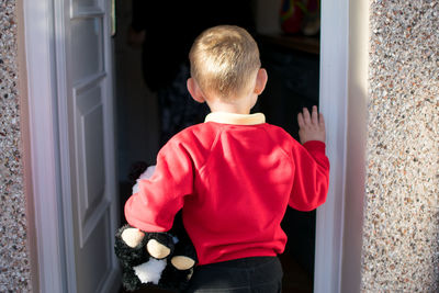 Rear view of boy with stuffed toy standing on doorway