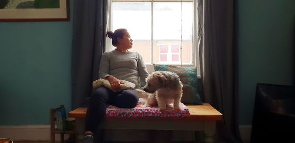 Woman with dog sitting by window at home