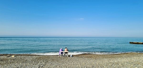 People looking at sea against clear sky