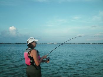 Woman fishing at river against sky