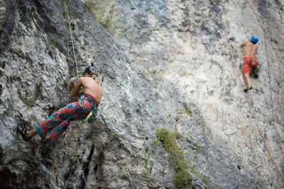 Low angle view of shirtless men climbing on rock formation