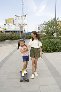 Girl teaching longboard skating to sister on footpath