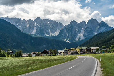 Road by houses and mountains against sky