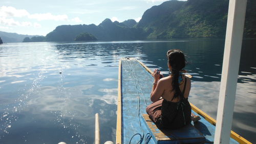 Rear view of shirtless man standing on lake against mountains