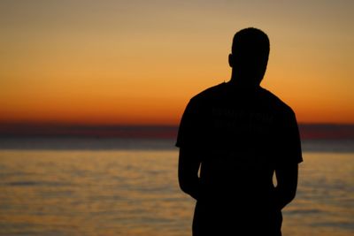 Silhouette man standing on beach against orange sky