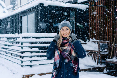 Portrait of attractive caucasian woman standing under snowfall in jacket and scarf.