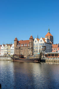 Buildings by river against clear blue sky
