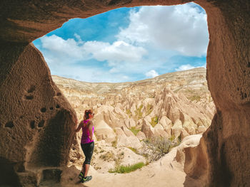 Rear view of woman standing by rock formation against sky