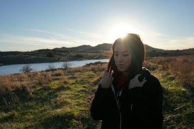 Young woman standing on grassy field against sky