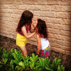 Cute girl embracing while standing by wall outdoors