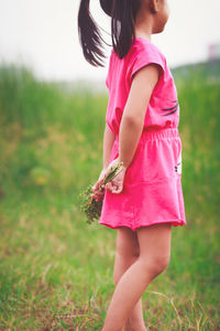 Midsection of girl holding plants while standing on field