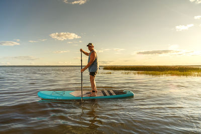 Rear view of woman standing on boat in sea against sky during sunset