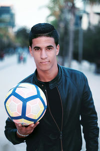 Portrait of man holding soccer ball while standing outdoors