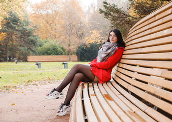 Young woman sitting on seat against trees