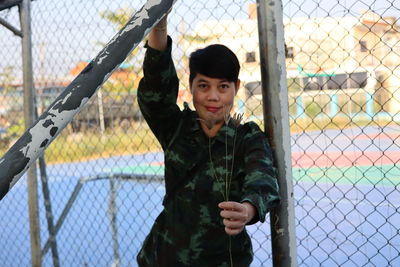 Portrait of man standing by chainlink fence