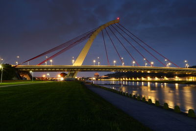 Illuminated bridge over river against sky at night