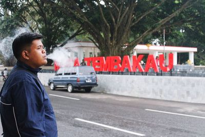 Side view of man smoking while standing by road in city