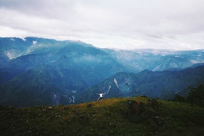 Rear view of man jumping on mountain against cloudy sky