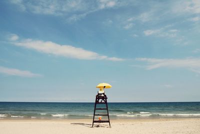 Lifeguard sitting on chair at beach against sky