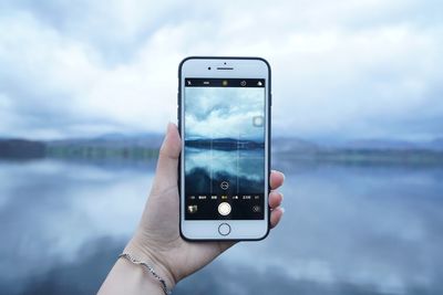 Close-up of hand holding smart phone against sky