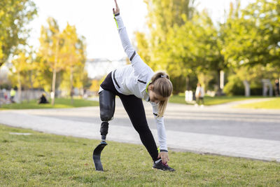 Focused paralympic female runner with leg prosthesis stretching body and doing forward bend during training