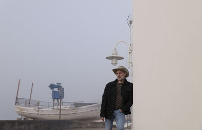 Portrait of adult man in cowboy hat and jeans against wall with fishing boat in background. almeria
