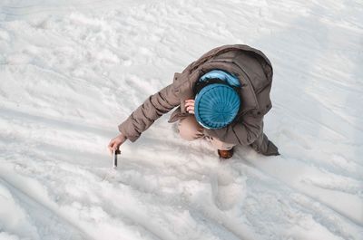 High angle view of young woman taking selfie while crouching on snow covered field