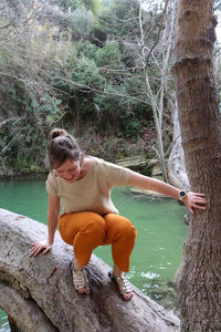 Full length of woman crouching on tree trunk in forest