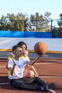 Love under sky,  close cuddle between mother and teen daughter and son outdoors on basketball court