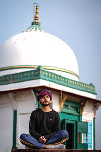 Portrait of man sitting against temple against sky
