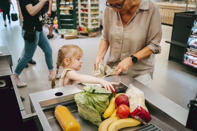 Girl helping grandmother filling groceries in bag at checkout in supermarket