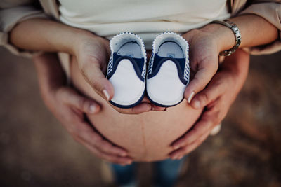 Low section of pregnant woman with man holding shoes while standing outdoors