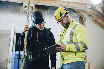 Male construction workers discussing over digital tablet while working at site