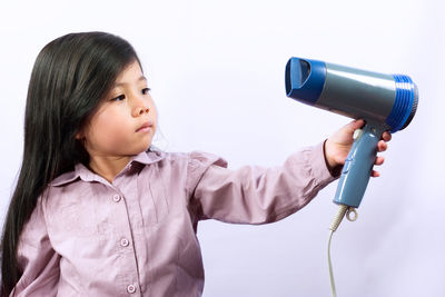 Close-up of cute girl holding hair dryer against white background