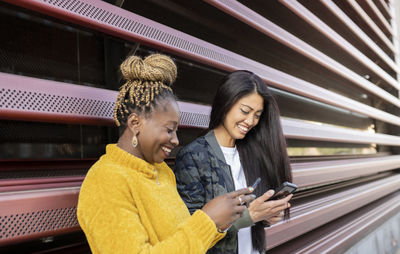 Female friends using smart phone by wall