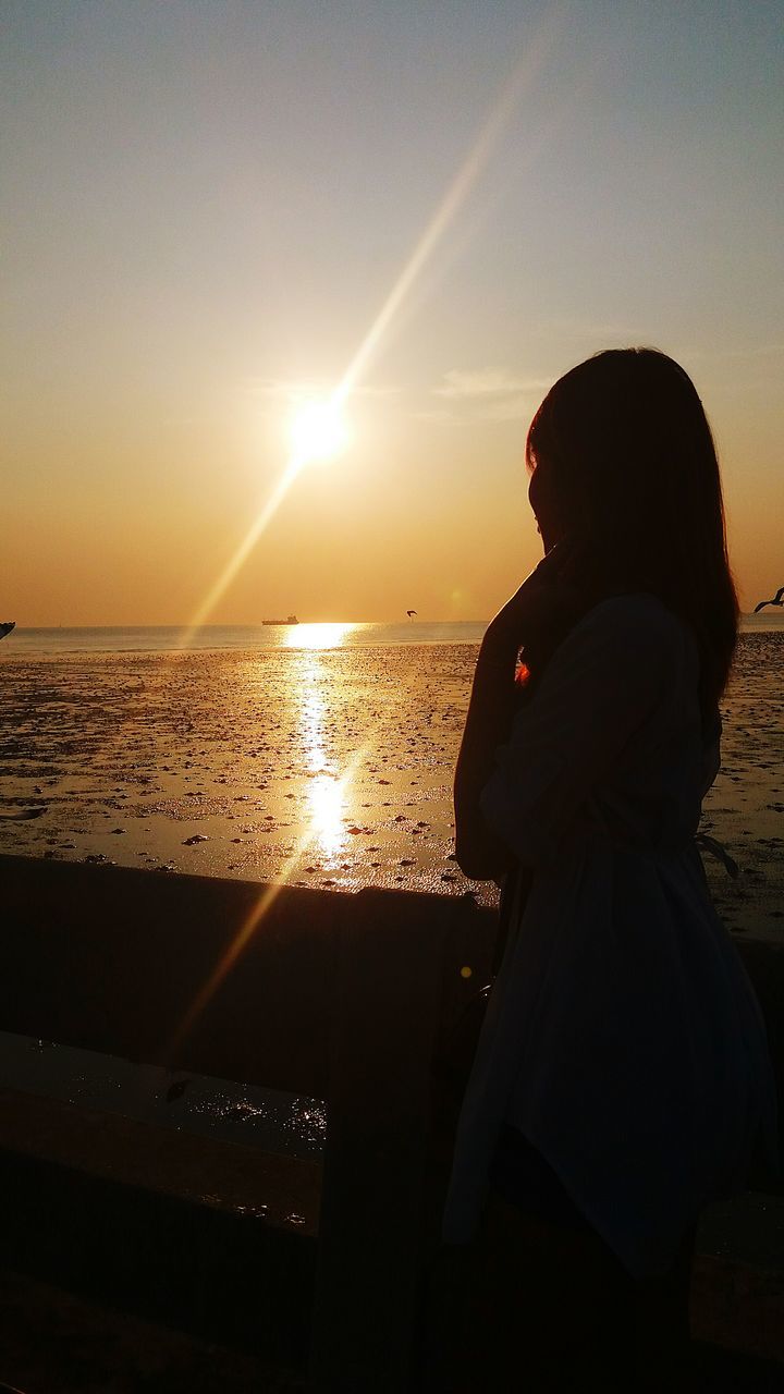 sunset, silhouette, sun, lifestyles, leisure activity, sky, sea, water, standing, sunlight, built structure, men, architecture, rear view, person, lens flare, horizon over water, beach