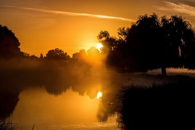 Silhouette trees by lake against sky during sunset