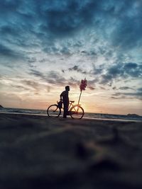 Rear view of man riding bicycles on beach against sky during sunset