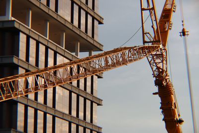 Low angle view of crane at construction site against sky in city