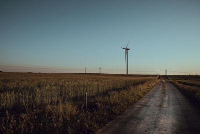 Road amidst field against clear sky. windmill