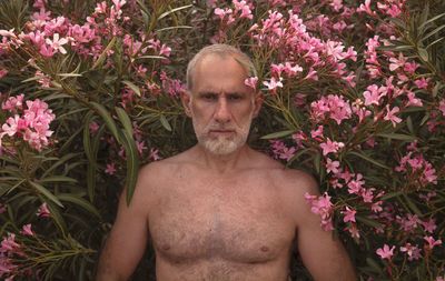 Portrait of shirtless man standing against flowers plants