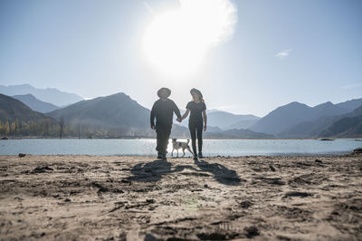 Couple holding hands while walking outdoors with natural landscape of mountains and lake.