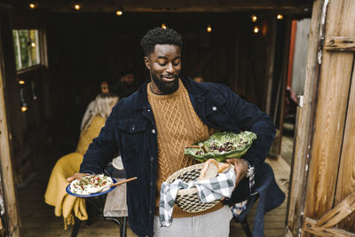 Smiling man balancing food while standing at doorway during social gathering