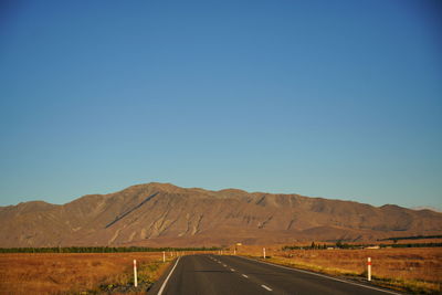 Road leading towards mountains against clear blue sky