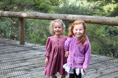 Portrait of smiling sisters standing on footbridge